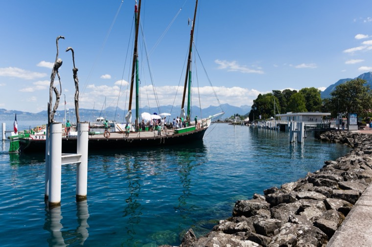 Port sur le lac Léman avec une barque traditionnelle, les montagnes en arrière-plan