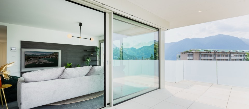 Terrasse avec baie vitrée toute hauteur et garde-corps en verre face au lac et aux montagnes