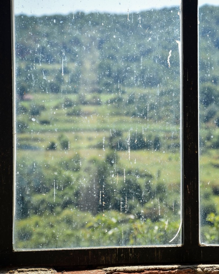 Vitre marquée par le calcaire et les traces de pluie devant un paysage de collines